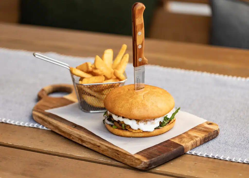 Auf einem Holzbrett liegt ein Burger mit mit Pommes