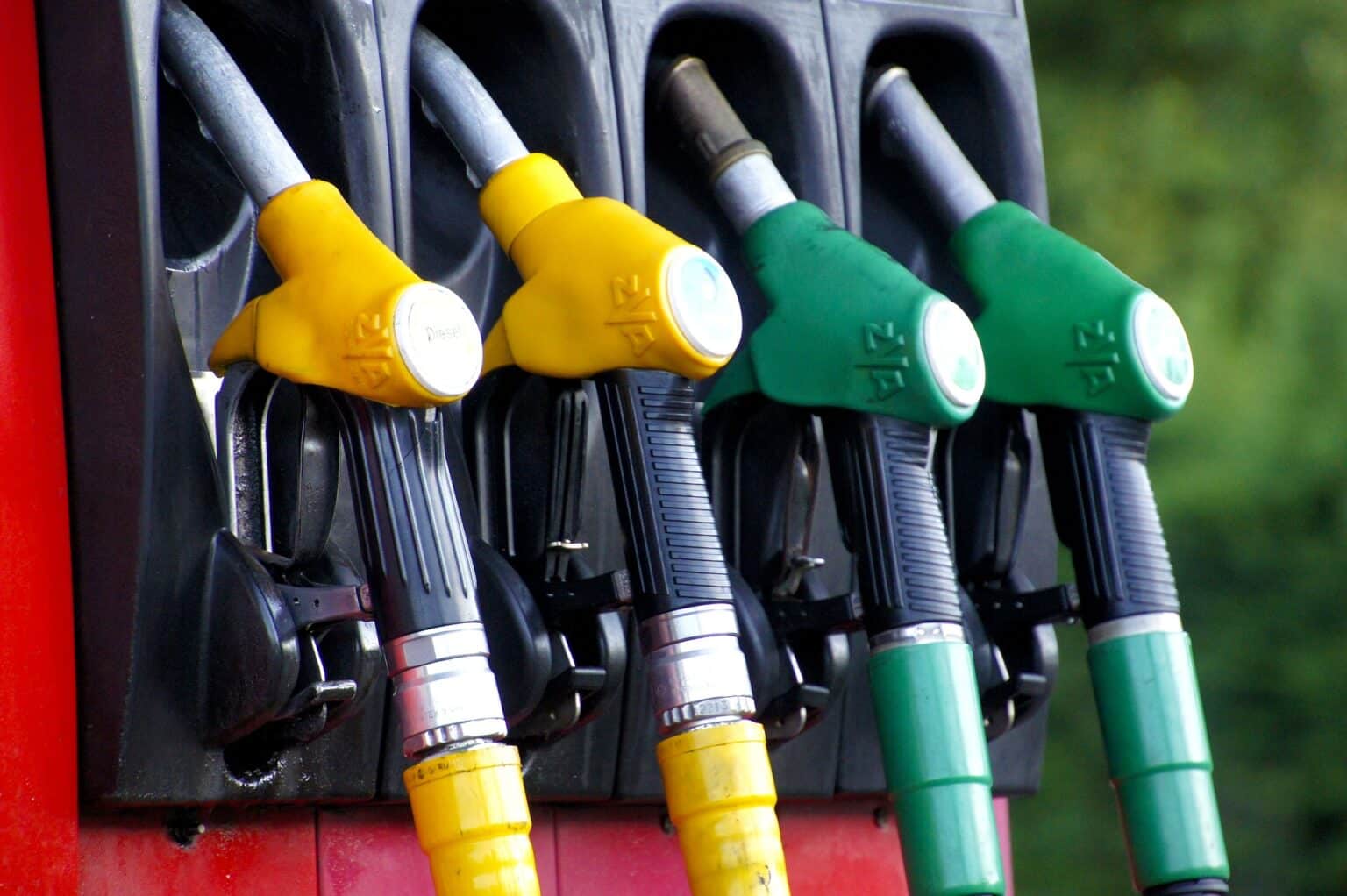 vier Zapfpistolen an einer Tankstelle, zwei gelbe für Diesel und zwei grüne für Benzin, in Halterungen steckend