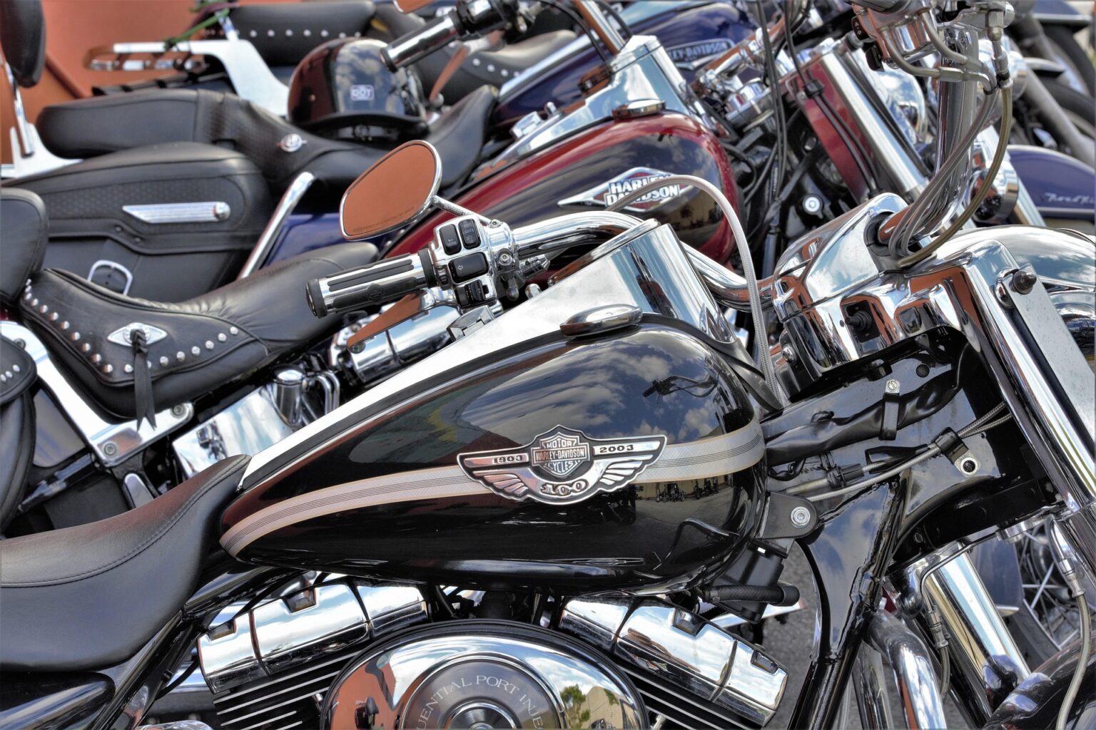 Schwarzes Harley-Davidson Motorrad mit glänzendem Tank, chromglänzenden Teilen und Nietenledersitz, Nahaufnahme von Tank und Lenker.